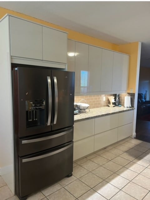 kitchen featuring black fridge, light tile patterned floors, white cabinets, and decorative backsplash