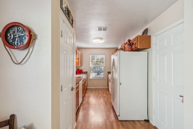 kitchen featuring white fridge, a textured ceiling, and light hardwood / wood-style flooring