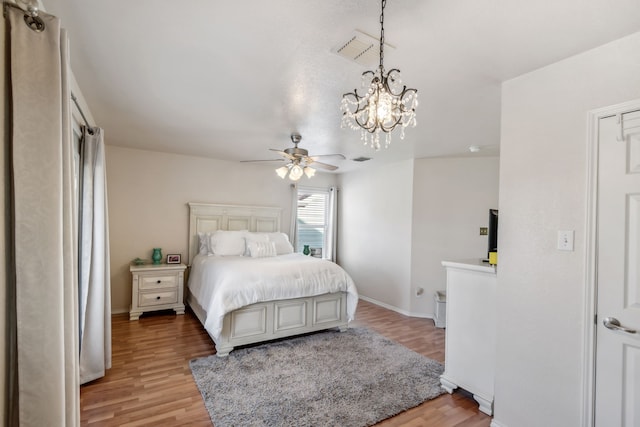 bedroom featuring ceiling fan with notable chandelier and light wood-type flooring