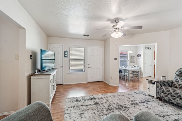 living room with ceiling fan, a textured ceiling, and light wood-type flooring