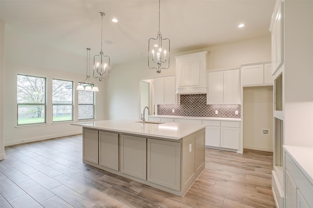 kitchen with light wood-type flooring, white cabinetry, decorative light fixtures, sink, and a kitchen island with sink