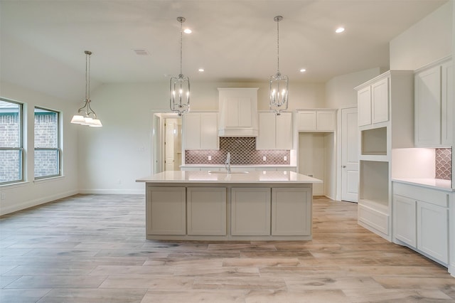 kitchen featuring tasteful backsplash, visible vents, a sink, white cabinetry, and a kitchen island with sink