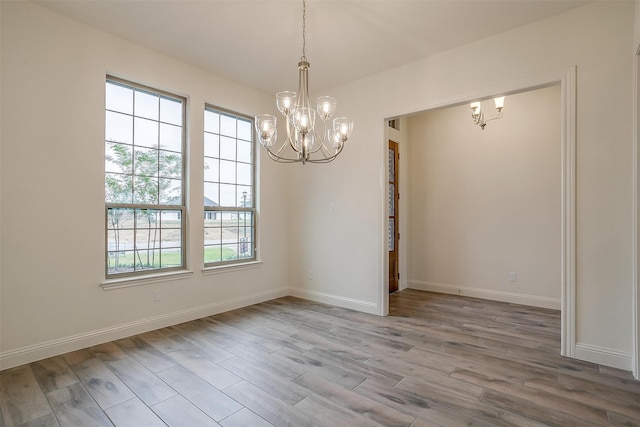 unfurnished room with baseboards, a notable chandelier, and wood finished floors