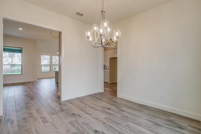 spare room with light wood-type flooring and a notable chandelier