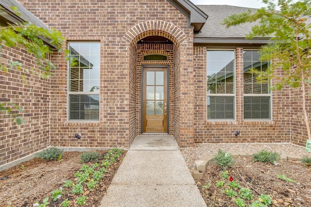 entrance to property featuring brick siding and a shingled roof