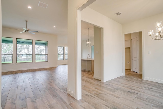 spare room with light wood-style flooring, ceiling fan with notable chandelier, visible vents, and a sink