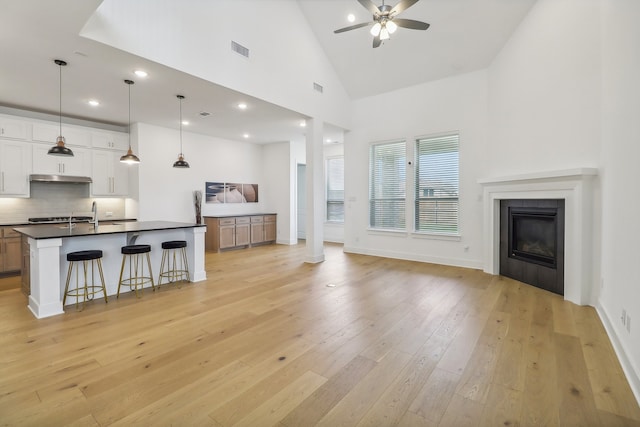 living room featuring ornate columns, high vaulted ceiling, light hardwood / wood-style floors, a tile fireplace, and ceiling fan