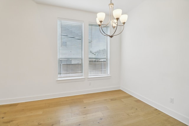 spare room featuring a chandelier, plenty of natural light, and light hardwood / wood-style flooring