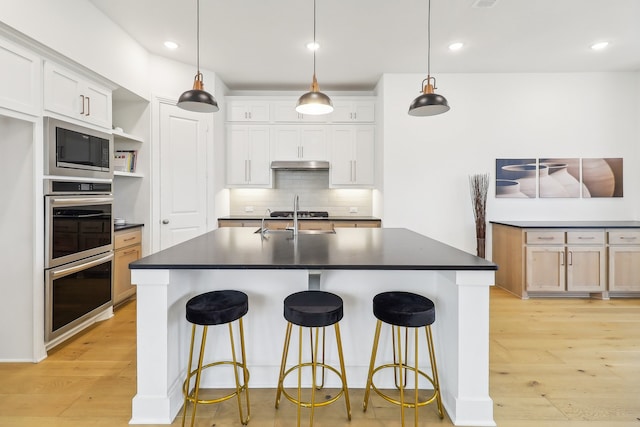 kitchen featuring white cabinets, hanging light fixtures, and a kitchen island with sink