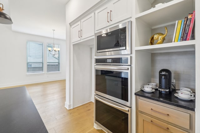 kitchen with stainless steel appliances, light hardwood / wood-style floors, white cabinets, hanging light fixtures, and tasteful backsplash