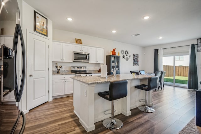 kitchen featuring white cabinetry, appliances with stainless steel finishes, dark hardwood / wood-style flooring, a kitchen breakfast bar, and a kitchen island with sink