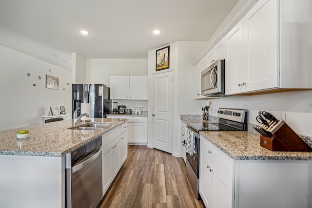 kitchen with stainless steel appliances, white cabinetry, light stone counters, an island with sink, and wood-type flooring