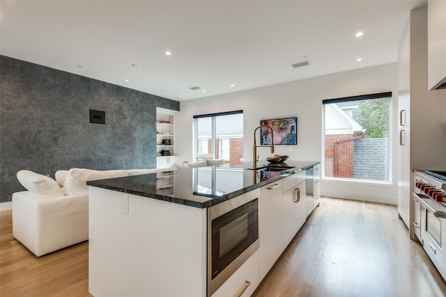 kitchen with stainless steel appliances, a healthy amount of sunlight, a kitchen island with sink, and white cabinetry