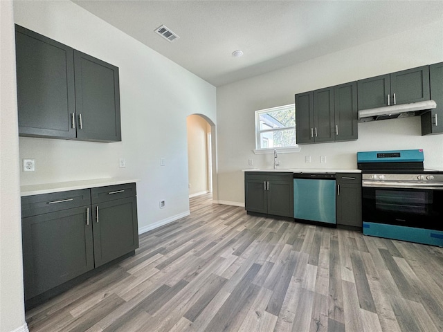 209 Smith St, Hillsboro, TX 76645 - kitchen featuring appliances with stainless steel finishes, arched walkways, light wood-style flooring, under cabinet range hood, and a sink