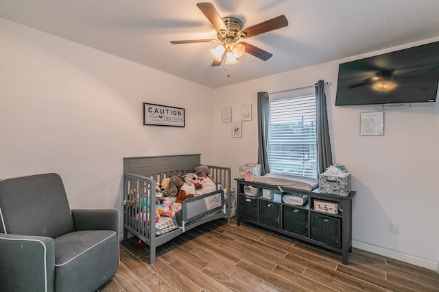 bedroom with hardwood / wood-style flooring, a nursery area, and ceiling fan