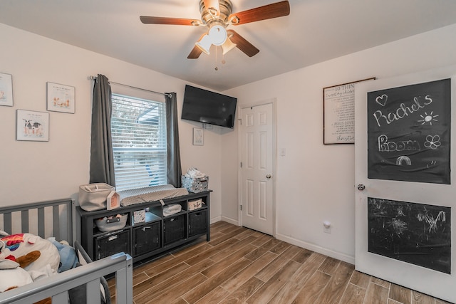 bedroom with a crib, hardwood / wood-style flooring, and ceiling fan