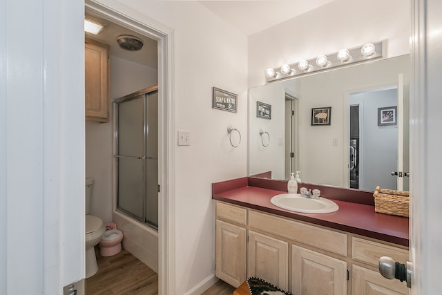 full bathroom featuring hardwood / wood-style flooring, vanity, combined bath / shower with glass door, and toilet