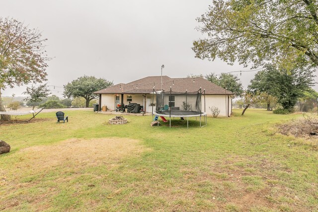 exterior space with an outdoor fire pit, a trampoline, and a yard