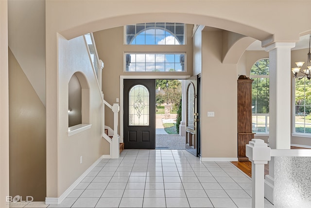 foyer featuring a towering ceiling, a notable chandelier, light tile patterned flooring, and decorative columns