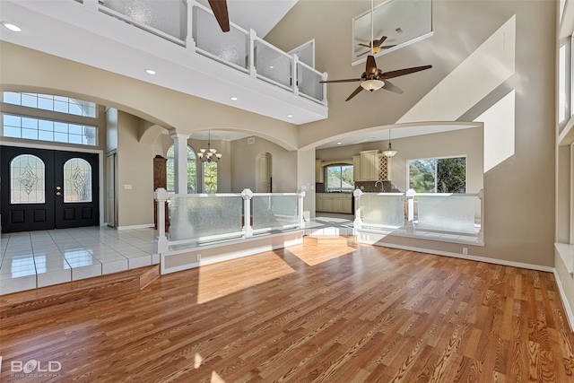 foyer entrance with french doors, high vaulted ceiling, light hardwood / wood-style floors, and ceiling fan with notable chandelier