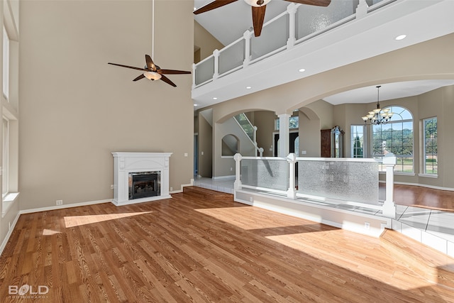 unfurnished living room featuring ornate columns, a towering ceiling, ceiling fan with notable chandelier, and hardwood / wood-style floors