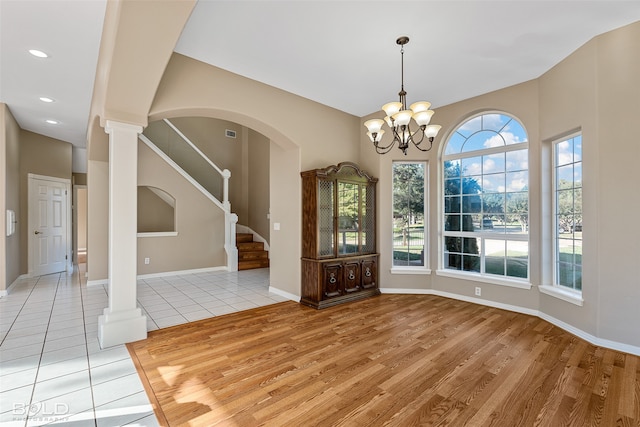 unfurnished dining area featuring ornate columns, a chandelier, and light hardwood / wood-style floors