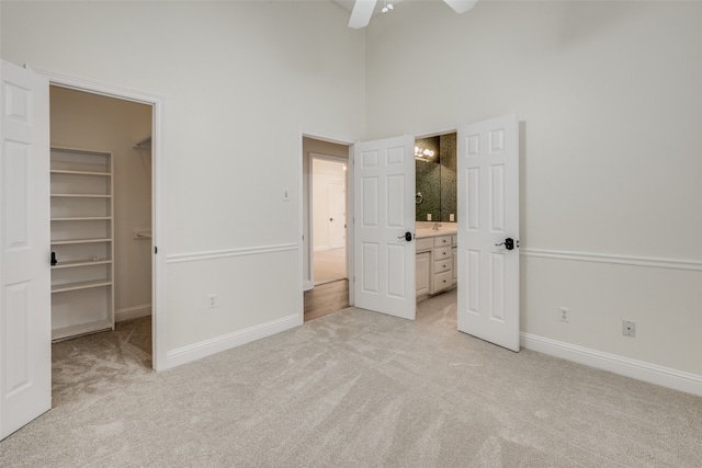 unfurnished bedroom with a high ceiling, ceiling fan, a walk in closet, light colored carpet, and a closet