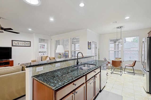 kitchen featuring stainless steel appliances, sink, dark stone counters, hanging light fixtures, and an island with sink