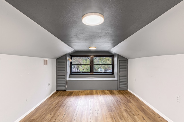 additional living space with a textured ceiling, light hardwood / wood-style flooring, and lofted ceiling