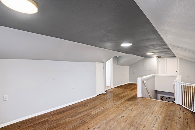 bonus room with wood-type flooring, lofted ceiling, and a textured ceiling