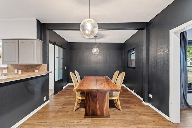 dining area with beam ceiling, a barn door, and light hardwood / wood-style flooring