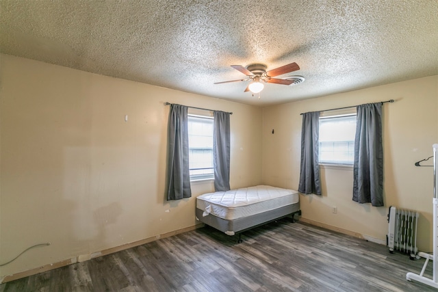 unfurnished bedroom featuring dark wood-type flooring, ceiling fan, a textured ceiling, and radiator heating unit