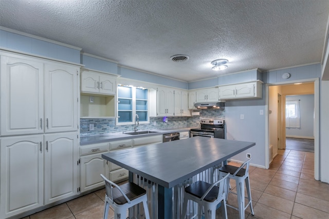 kitchen with appliances with stainless steel finishes, light tile patterned floors, sink, a kitchen breakfast bar, and white cabinets