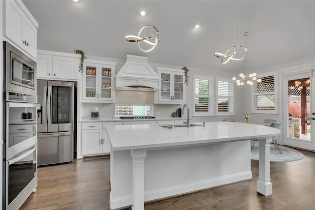 kitchen featuring premium range hood, white cabinetry, a chandelier, a kitchen island with sink, and stainless steel appliances