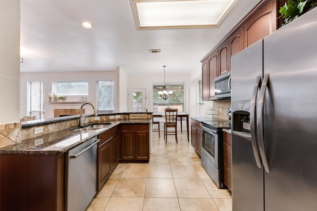 kitchen with stainless steel appliances, sink, dark stone counters, an inviting chandelier, and decorative light fixtures