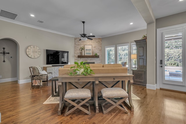 dining space with a stone fireplace, hardwood / wood-style floors, ornamental molding, and ceiling fan