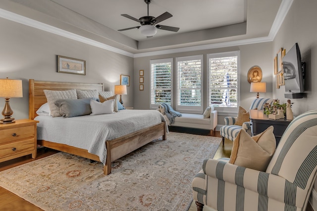 bedroom featuring hardwood / wood-style floors, ceiling fan, crown molding, and a tray ceiling