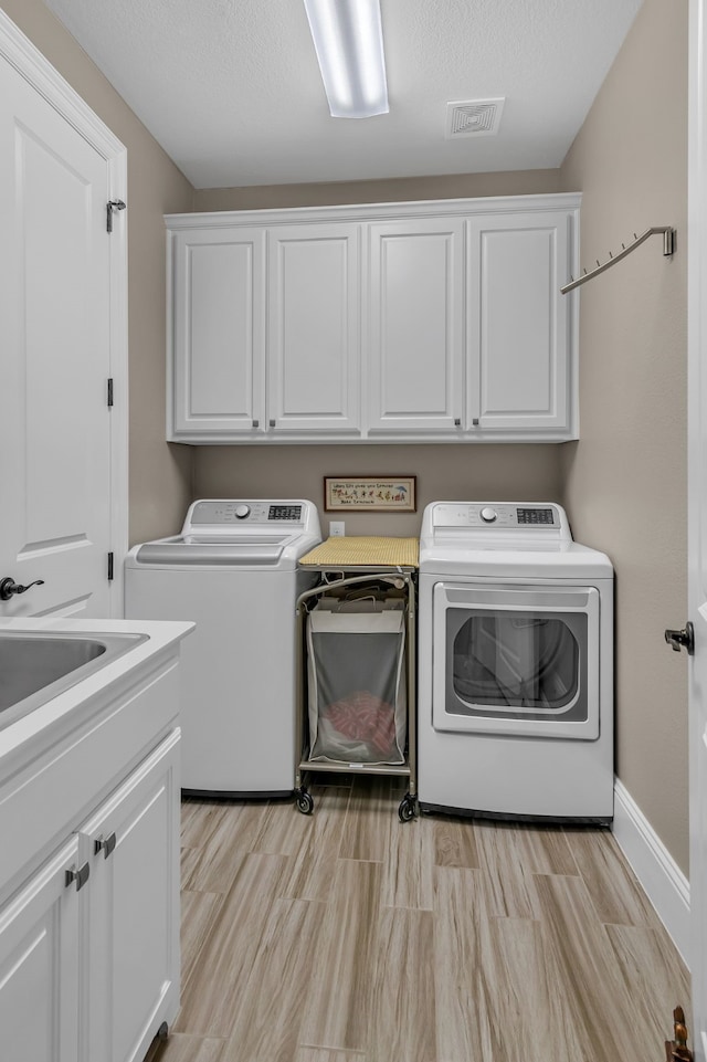 clothes washing area featuring cabinets, separate washer and dryer, a textured ceiling, and light wood-type flooring