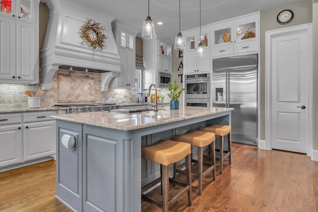 kitchen with built in appliances, a center island with sink, and light hardwood / wood-style flooring