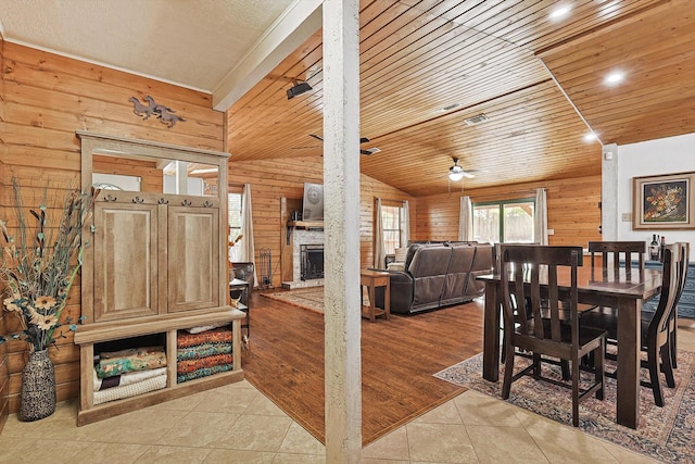 tiled dining room with ceiling fan, wood walls, a stone fireplace, and wood ceiling