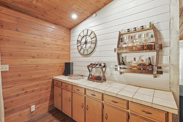 bar with tile countertops, wood walls, and lofted ceiling