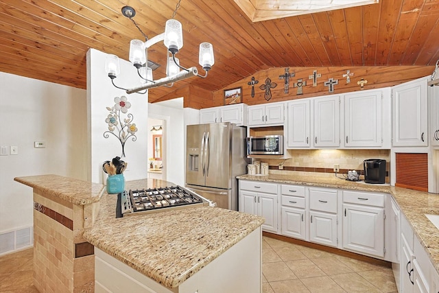 kitchen featuring hanging light fixtures, light stone counters, lofted ceiling with skylight, white cabinets, and appliances with stainless steel finishes