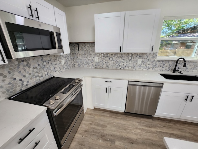 kitchen with white cabinetry, appliances with stainless steel finishes, backsplash, sink, and light hardwood / wood-style flooring