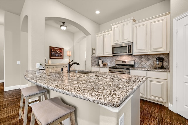 kitchen with light stone counters, backsplash, appliances with stainless steel finishes, sink, and dark wood-type flooring