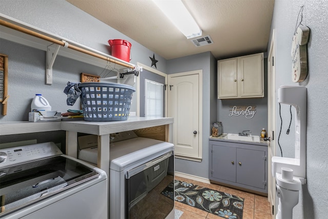 clothes washing area with cabinets, a textured ceiling, sink, washing machine and clothes dryer, and light tile patterned flooring