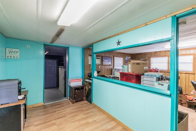 kitchen with wooden walls, light wood-type flooring, and a textured ceiling