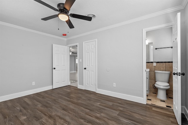 unfurnished bedroom featuring dark wood-type flooring, tile walls, ceiling fan, and ensuite bath