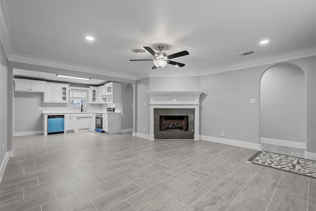 unfurnished living room featuring ornamental molding, a tiled fireplace, sink, ceiling fan, and light hardwood / wood-style flooring