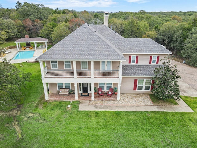 rear view of house with a lawn, a patio, and a balcony