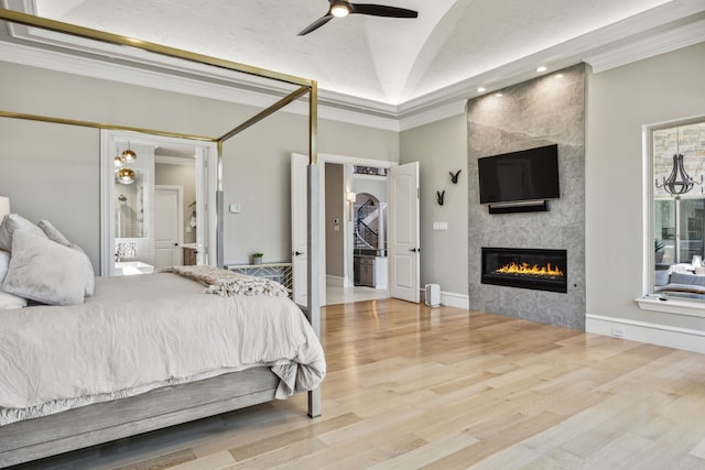 bedroom featuring light hardwood / wood-style floors, a tiled fireplace, ceiling fan, crown molding, and vaulted ceiling